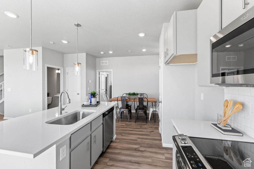 Kitchen with appliances with stainless steel finishes, recessed lighting, dark wood-style floors, light countertops, and a kitchen island with sink