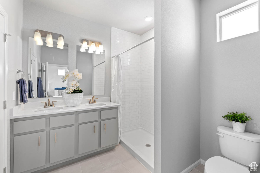 Bathroom featuring tiled shower, double vanity, and tile patterned floors