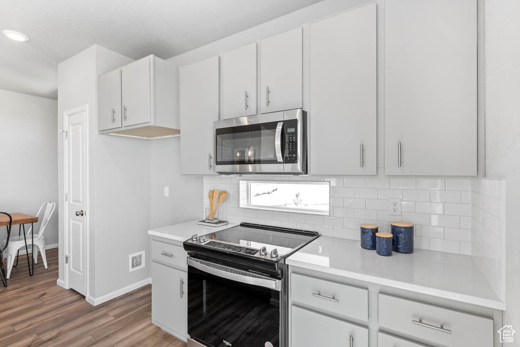 Kitchen featuring appliances with stainless steel finishes, light countertops, backsplash, light wood-type flooring, and recessed lighting