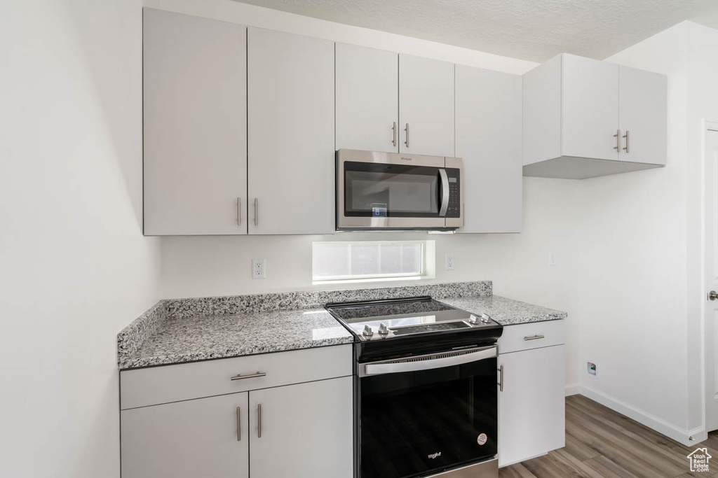 Kitchen with stainless steel appliances, light wood-type flooring, light stone counters, and white cabinetry