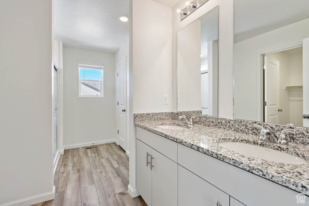 Bathroom with double vanity, wood finished floors, and a textured ceiling