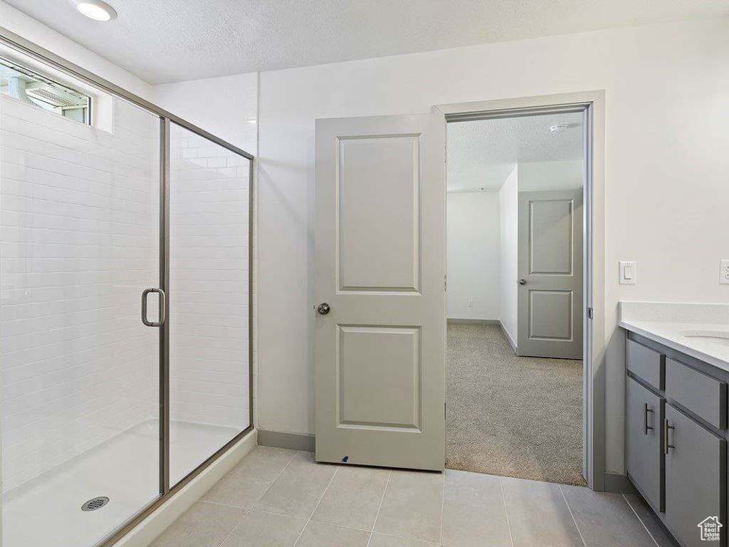 Full bath with vanity, a textured ceiling, a stall shower, and tile patterned flooring
