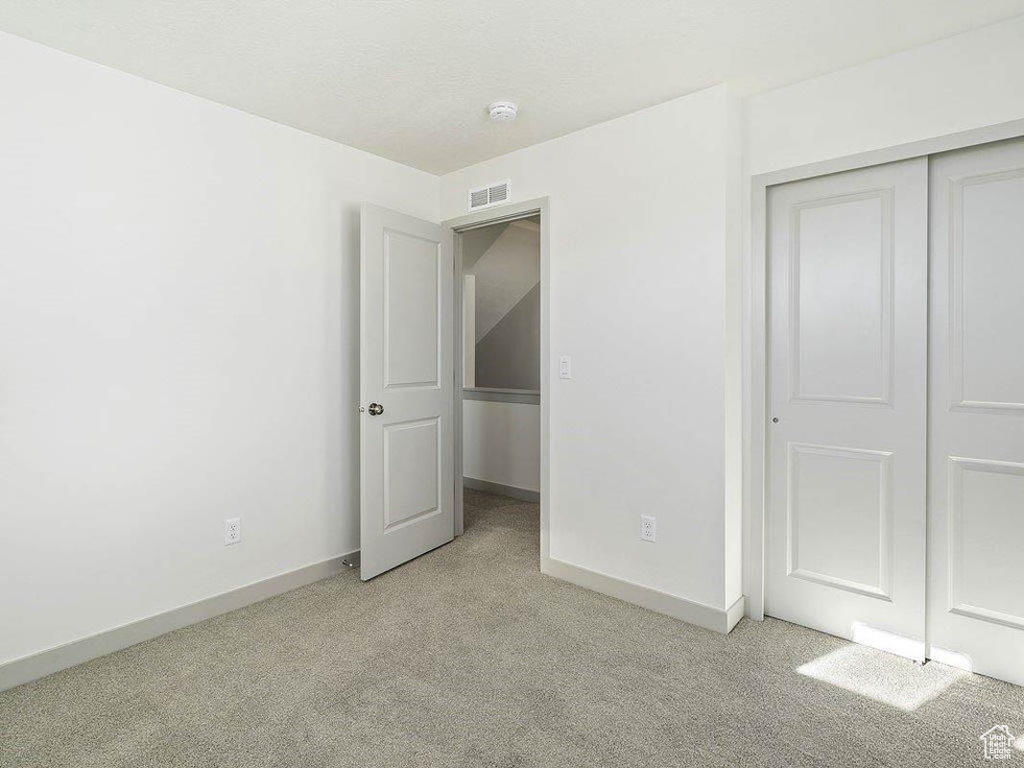 Unfurnished bedroom with light colored carpet and a closet