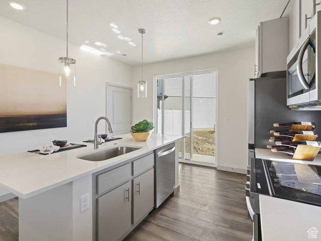 Kitchen featuring stainless steel appliances, dark wood-style flooring, light countertops, decorative light fixtures, and recessed lighting