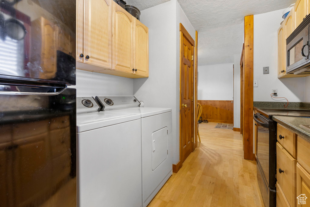 Laundry room with washer and clothes dryer, light wood-style floors, and a textured ceiling