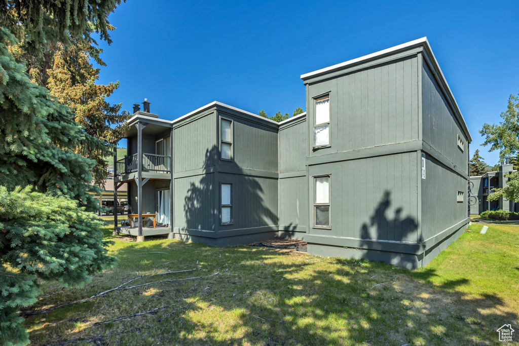 Rear view of property featuring a balcony, a lawn, and a chimney