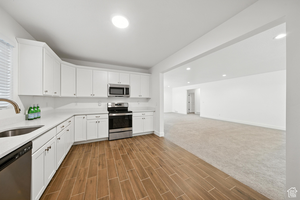 Kitchen featuring stainless steel appliances, light countertops, white cabinetry, recessed lighting, and wood finished floors