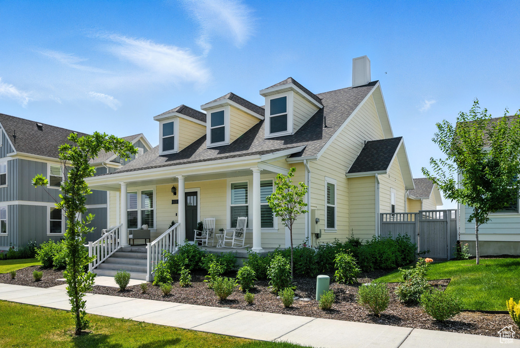 New england style home featuring a chimney, covered porch, and a shingled roof