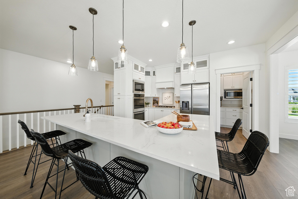 Kitchen featuring appliances with stainless steel finishes, wood finished floors, white cabinetry, recessed lighting, and a breakfast bar area