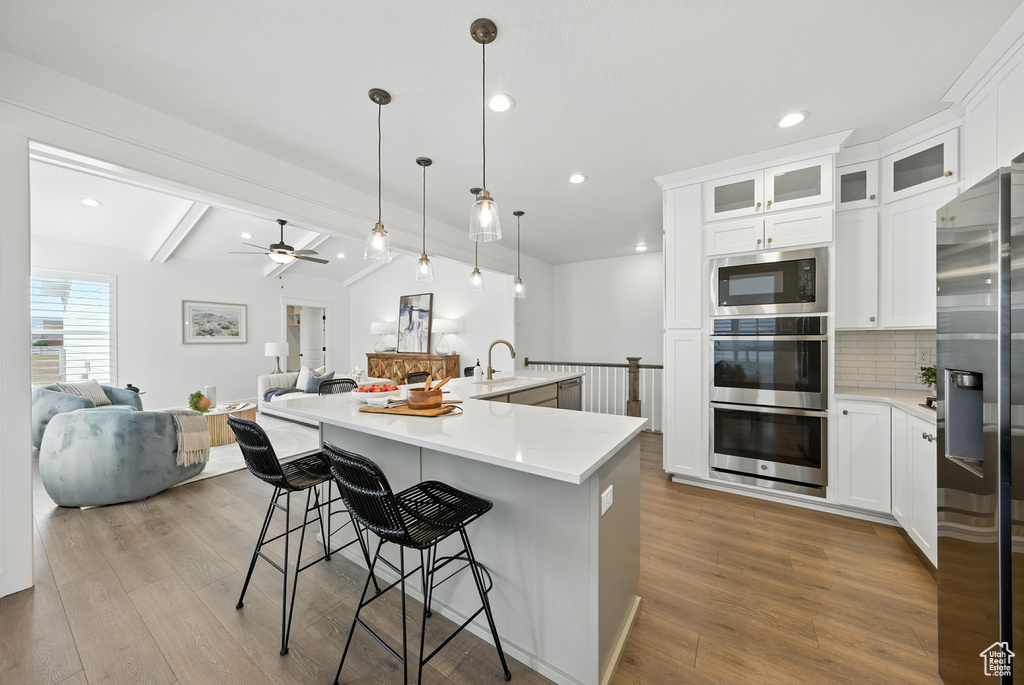 Kitchen with stainless steel appliances, open floor plan, tasteful backsplash, wood finished floors, and recessed lighting