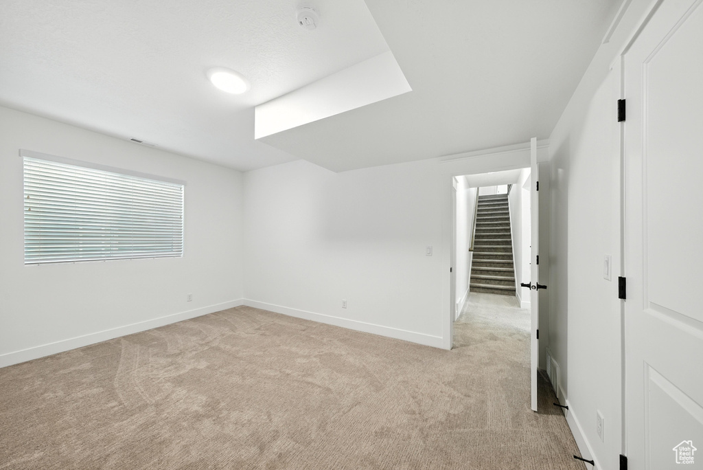 Empty room featuring light carpet, a smoke detector, and stairs