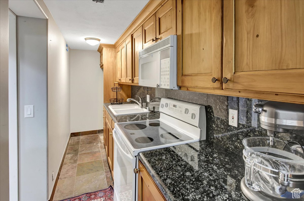 Kitchen with white appliances, tasteful backsplash, stone finish flooring, and dark stone counters