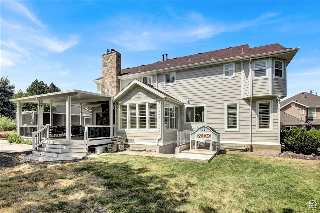 Back of property featuring a chimney, a lawn, and a sunroom