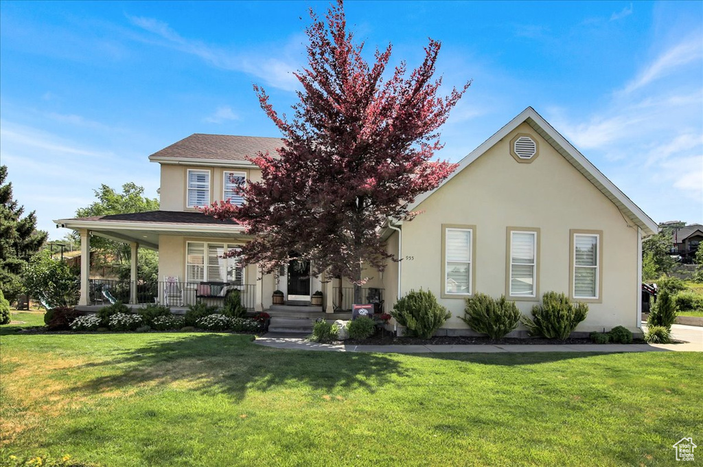 View of property hidden behind natural elements with a front lawn, stucco siding, and a porch