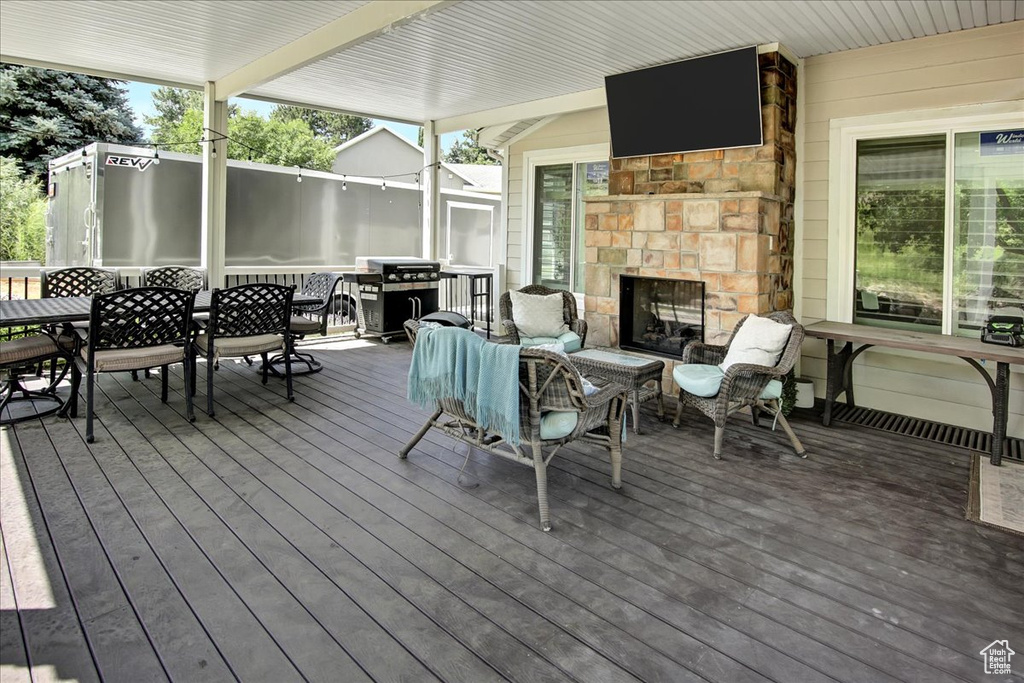 Wooden terrace featuring exterior fireplace, outdoor dining space, and grilling area