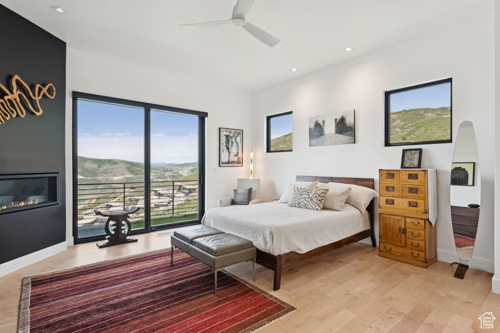 Bedroom featuring light wood-type flooring, access to outside, recessed lighting, a glass covered fireplace, and ceiling fan