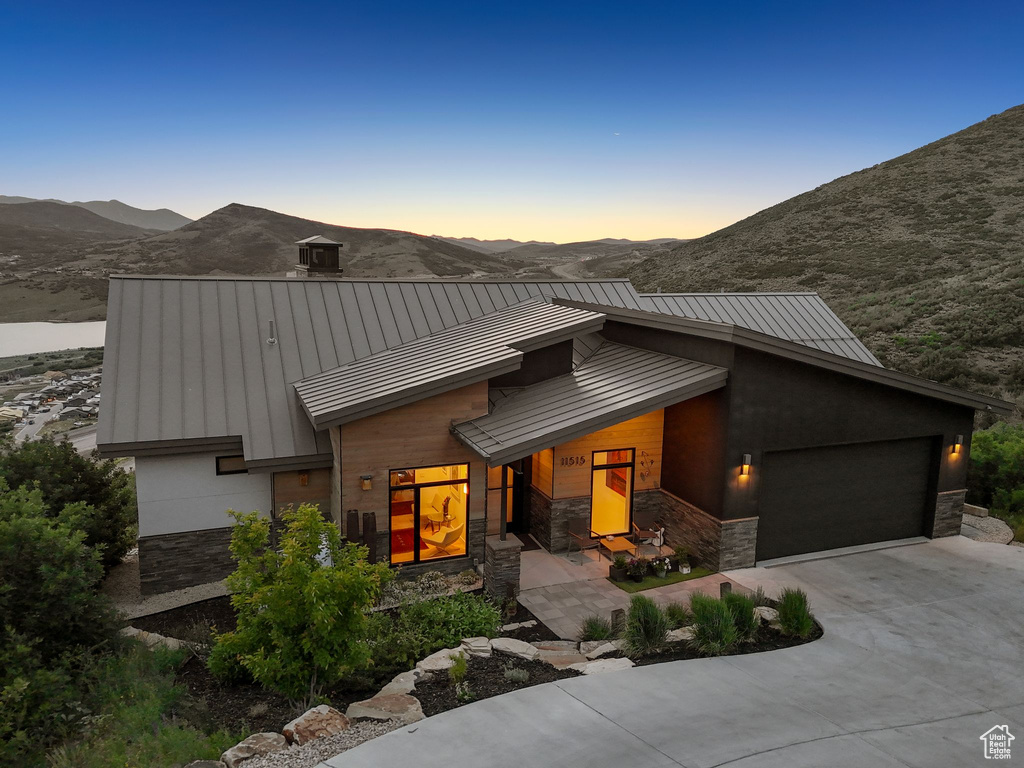 View of front of home with a standing seam roof, stone siding, an attached garage, and concrete driveway
