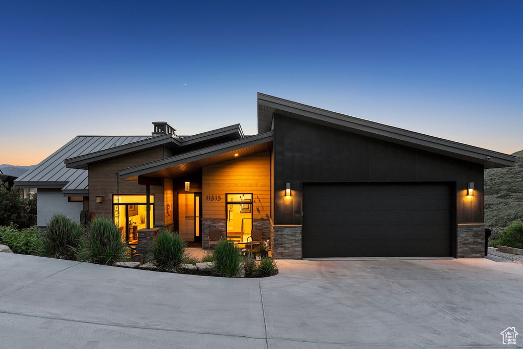 Modern home featuring a garage, driveway, a standing seam roof, stone siding, and a metal roof