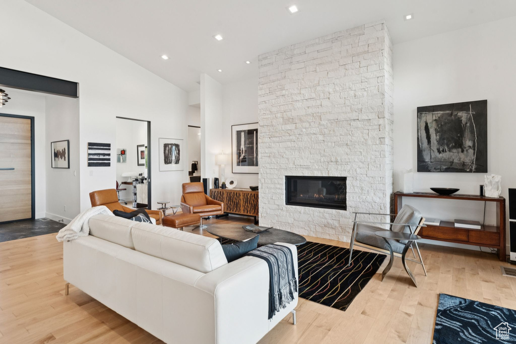 Living room with wood finished floors, high vaulted ceiling, a stone fireplace, and recessed lighting