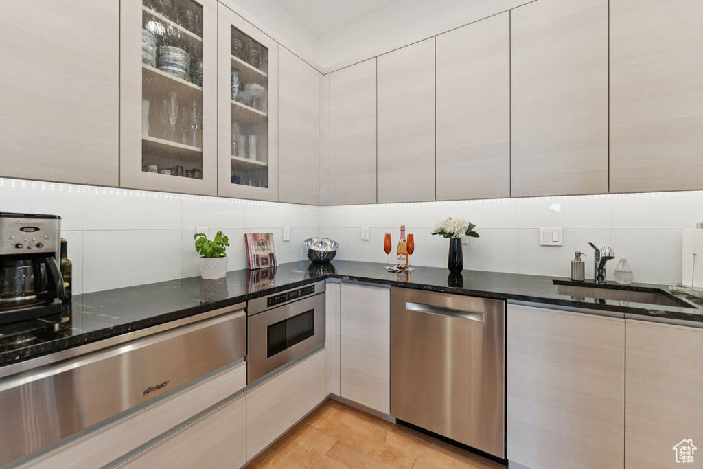 Kitchen with stainless steel dishwasher, a warming drawer, decorative backsplash, dark stone countertops, and modern cabinets