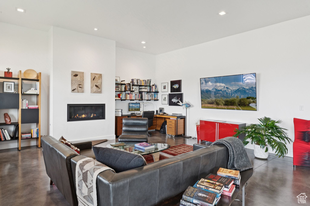 Living room with concrete floors, a glass covered fireplace, an office area, and recessed lighting
