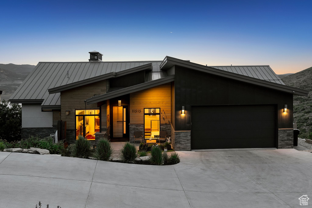 Modern home featuring a standing seam roof, an attached garage, concrete driveway, a metal roof, and stone siding