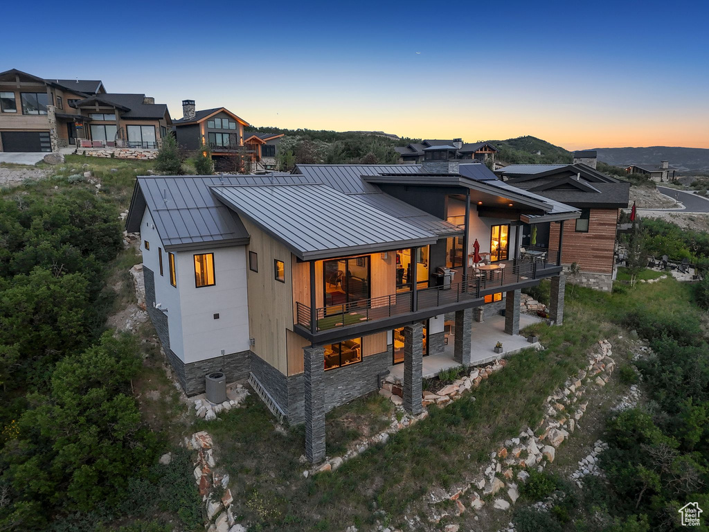 Back of property at dusk with a standing seam roof, a metal roof, a balcony, a patio, and stone siding