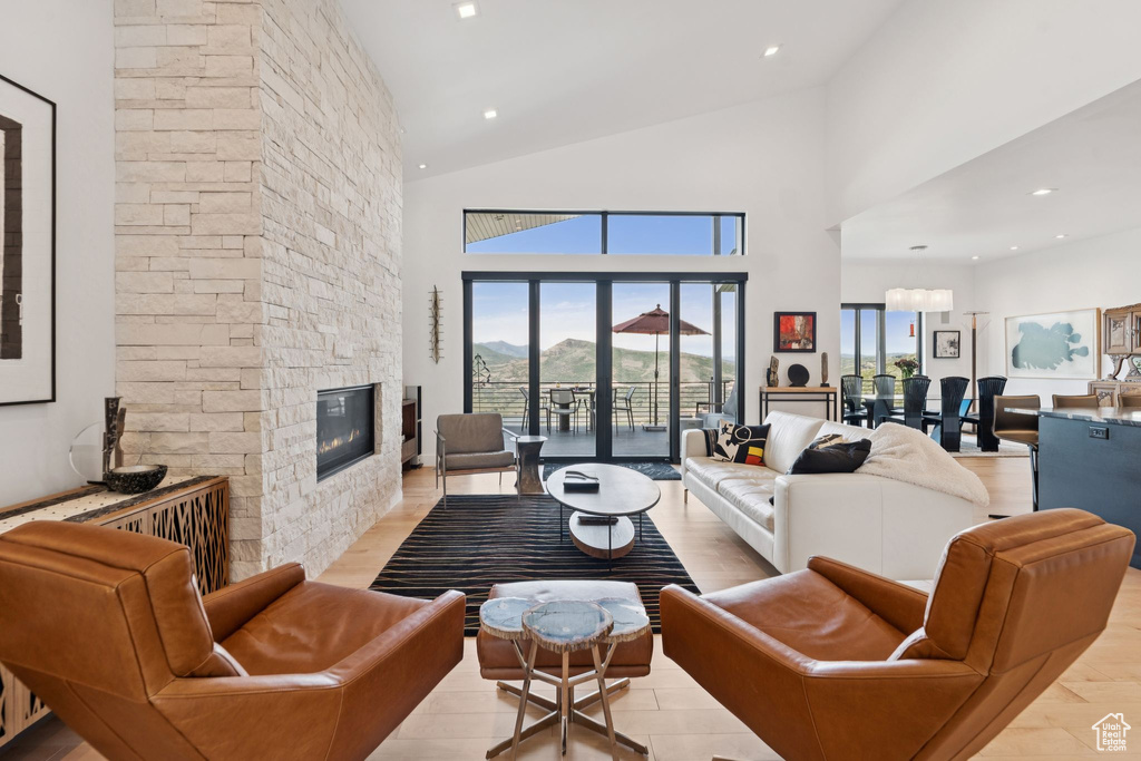Living area with healthy amount of natural light, a stone fireplace, high vaulted ceiling, and light wood-type flooring