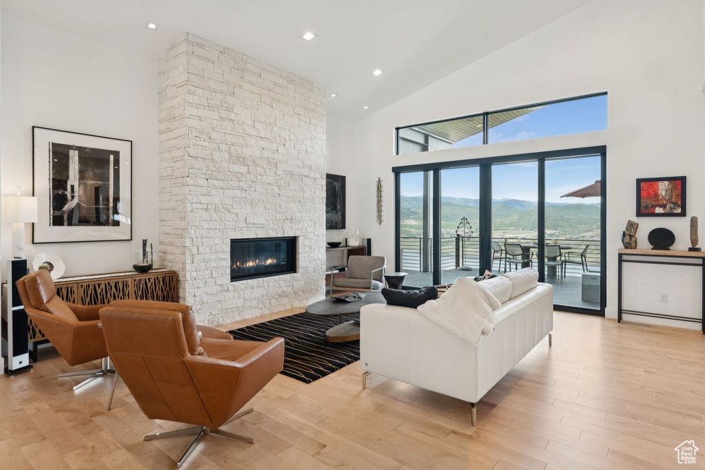 Living room featuring high vaulted ceiling, a stone fireplace, light wood-type flooring, and recessed lighting