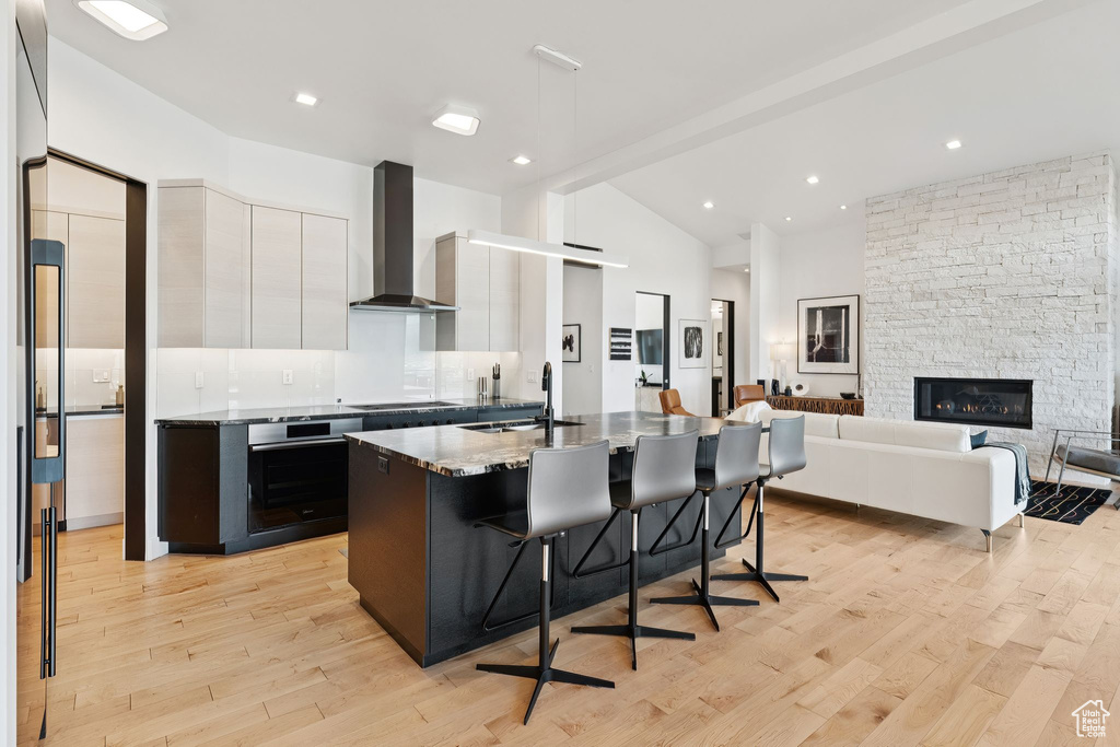 Kitchen with wall chimney exhaust hood, oven, white cabinetry, modern cabinets, and a breakfast bar area