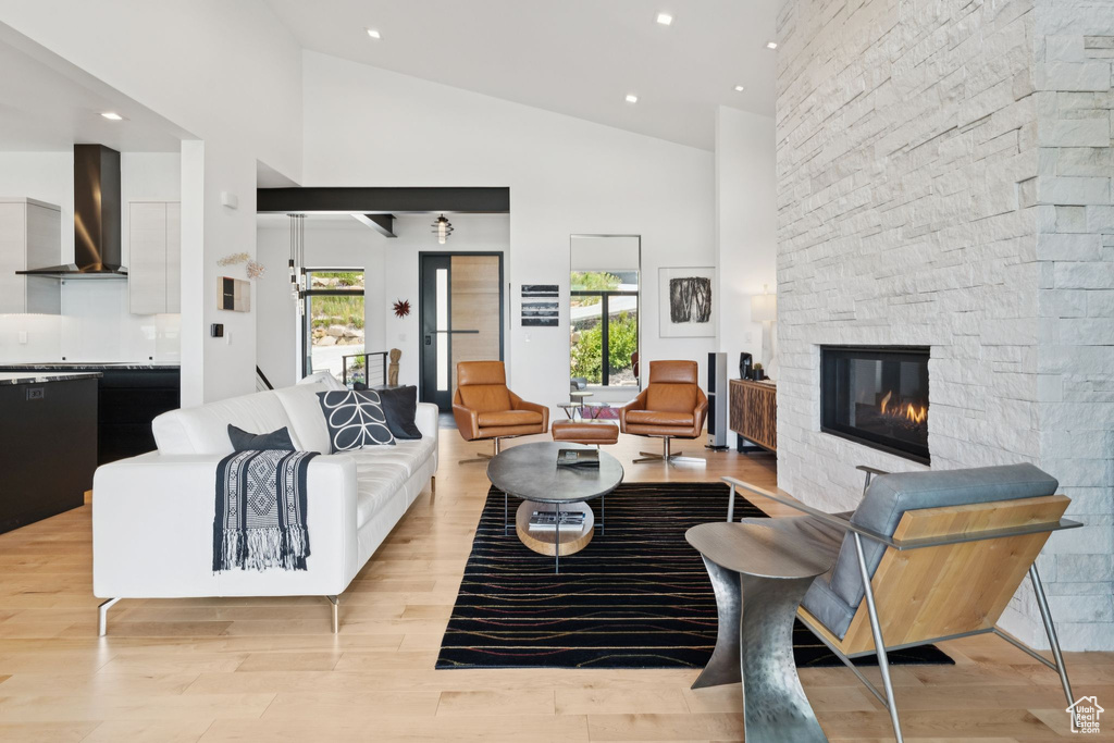 Living room featuring a stone fireplace, high vaulted ceiling, light wood-style flooring, and recessed lighting