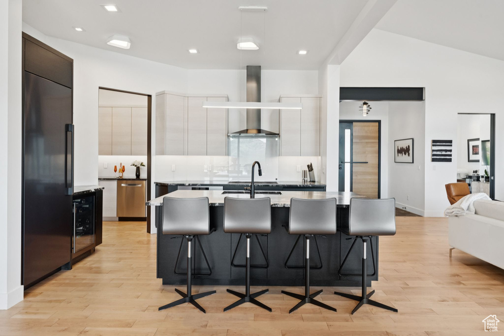 Kitchen with wall chimney exhaust hood, modern cabinets, wine cooler, light wood-type flooring, and recessed lighting