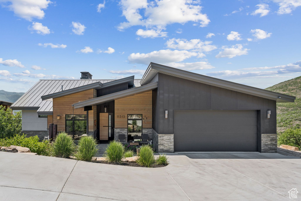 Contemporary house with stone siding, concrete driveway, a garage, a standing seam roof, and a metal roof