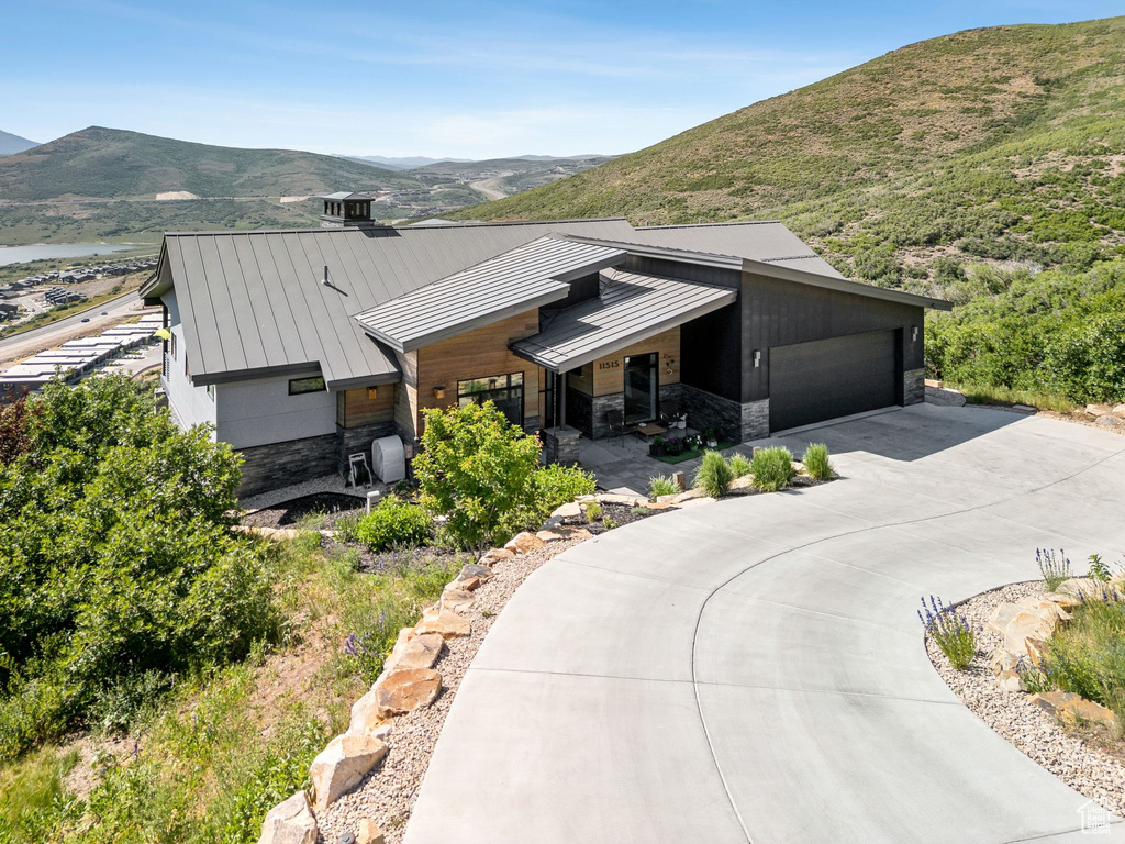 View of front of home featuring a standing seam roof, stone siding, driveway, and a mountain view