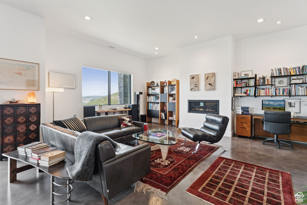 Living area featuring concrete floors, a glass covered fireplace, recessed lighting, and built in desk