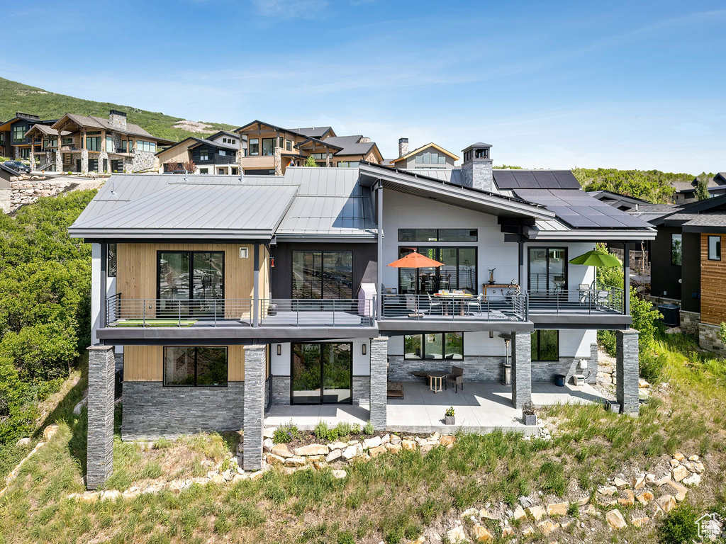 Rear view of property with a balcony, a patio, stone siding, and solar panels