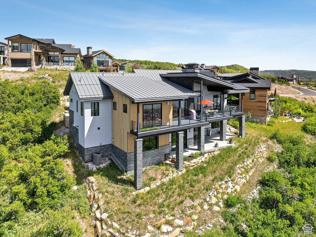 Back of house with a standing seam roof, a balcony, a metal roof, and a patio