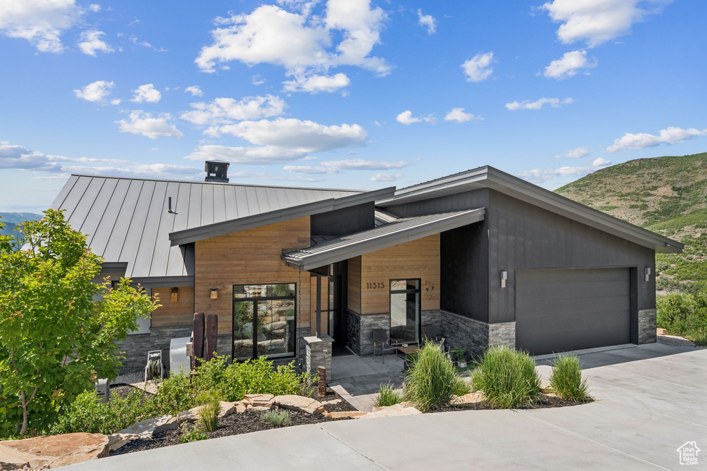 Contemporary home featuring a standing seam roof, stone siding, a mountain view, driveway, and a metal roof