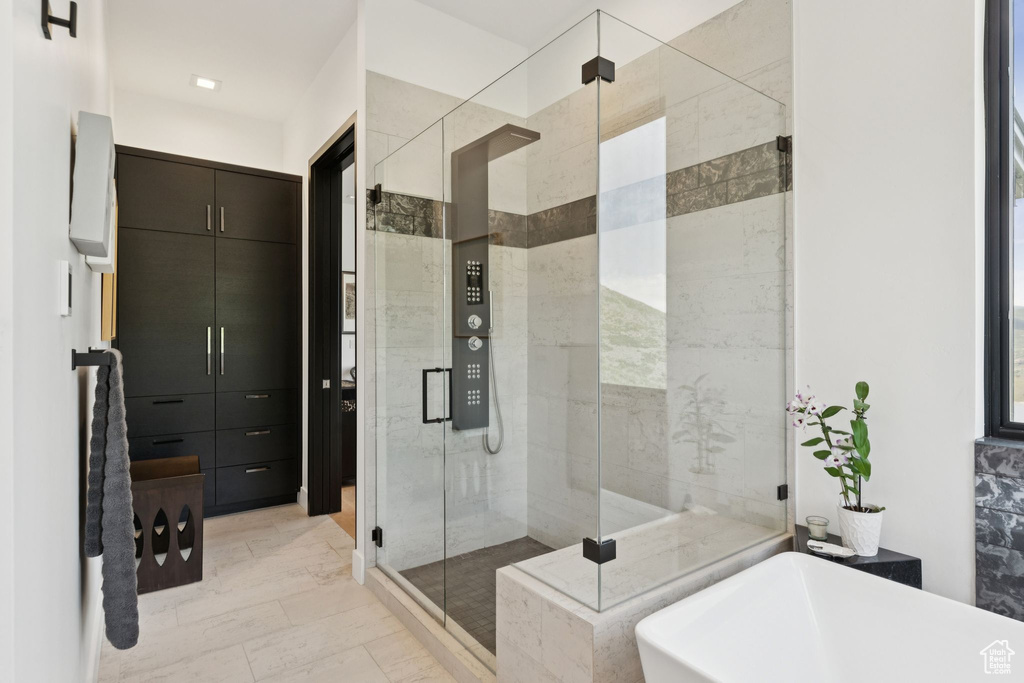 Bathroom with marble look tiles, a soaking tub, and a stall shower