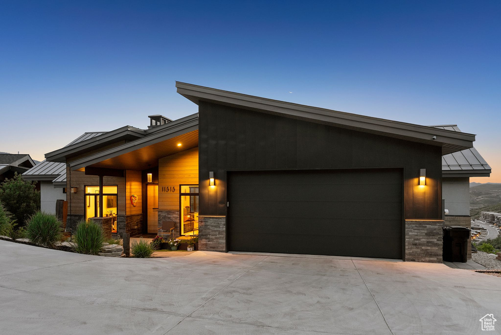 View of front of house featuring a standing seam roof, stone siding, an attached garage, and a metal roof