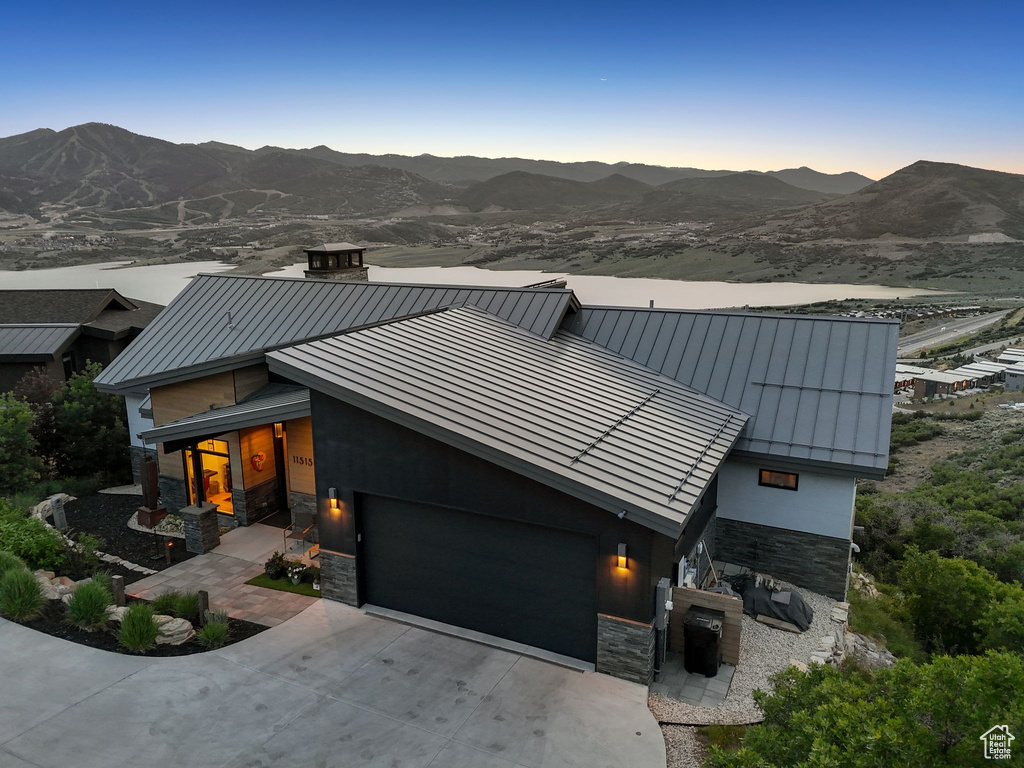 Modern home featuring a standing seam roof, stone siding, a garage, and driveway