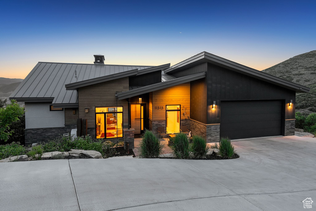 Contemporary home featuring a standing seam roof, stone siding, a garage, driveway, and a metal roof