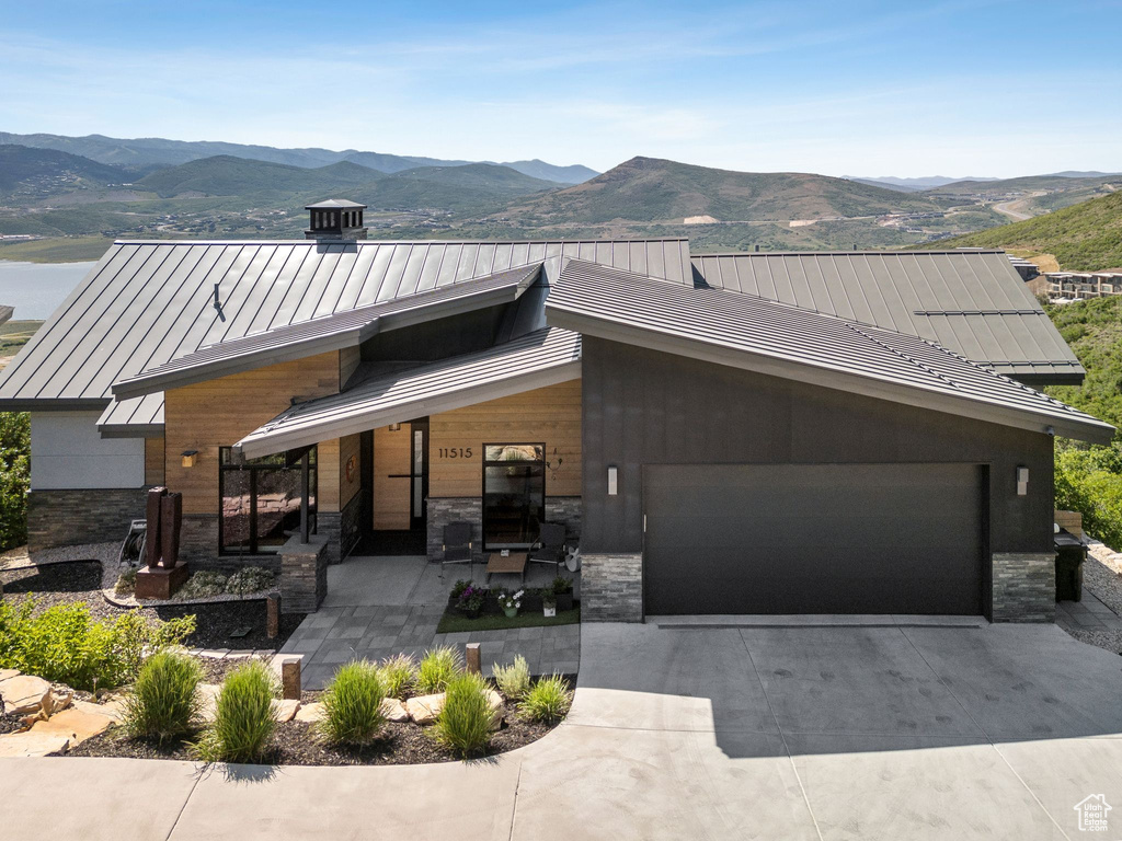View of front of house featuring a standing seam roof, a mountain view, an attached garage, stone siding, and driveway
