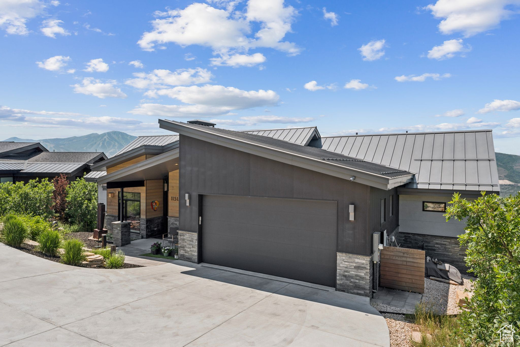 Contemporary house with a standing seam roof, an attached garage, a metal roof, driveway, and stone siding