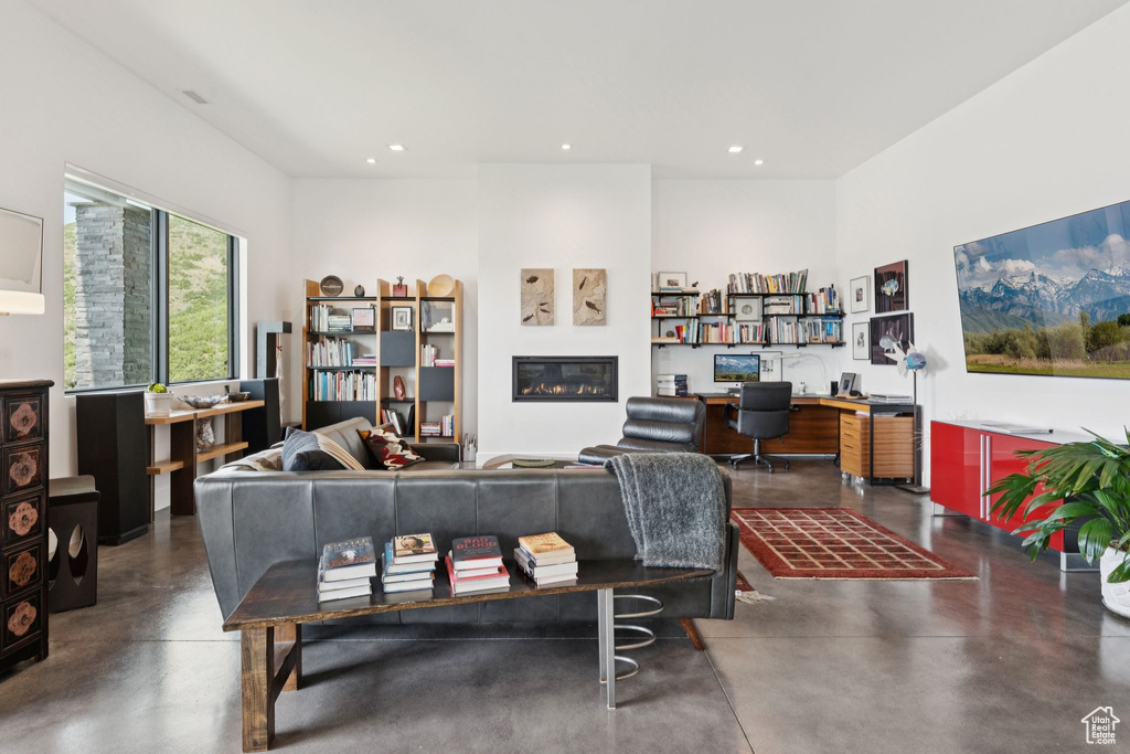 Living room with finished concrete floors, recessed lighting, a glass covered fireplace, and built in desk