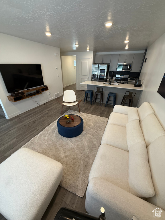 Living area featuring dark wood-type flooring, a textured ceiling, and recessed lighting