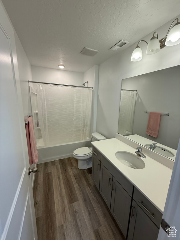 Bathroom featuring vanity, shower / bathtub combination with curtain, wood finished floors, and a textured ceiling