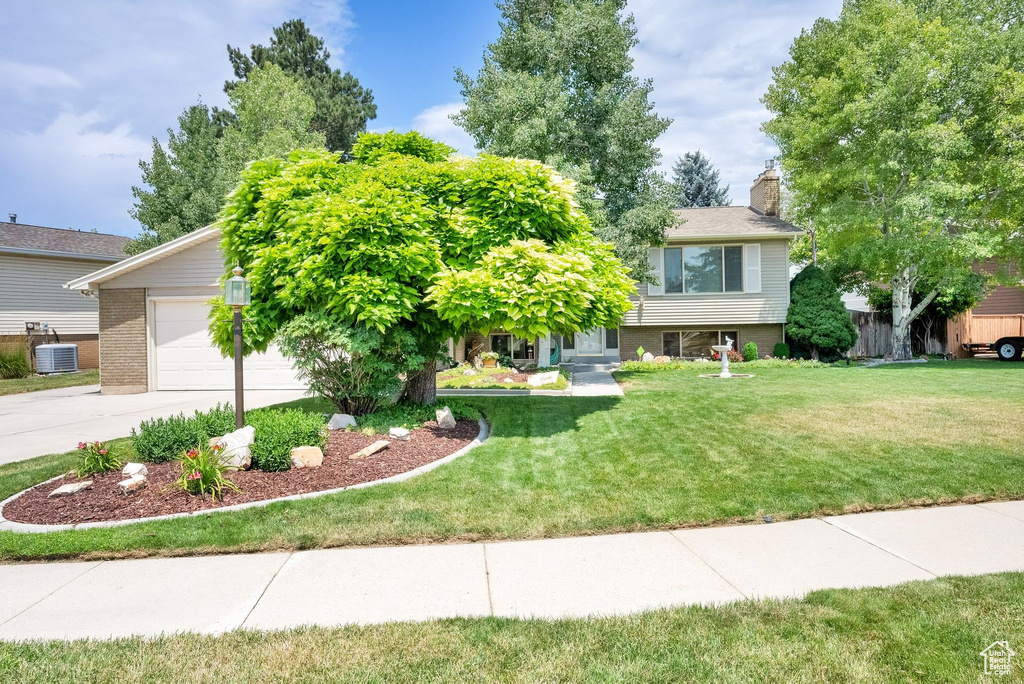 View of front of property with brick siding, concrete driveway, a chimney, and a front yard