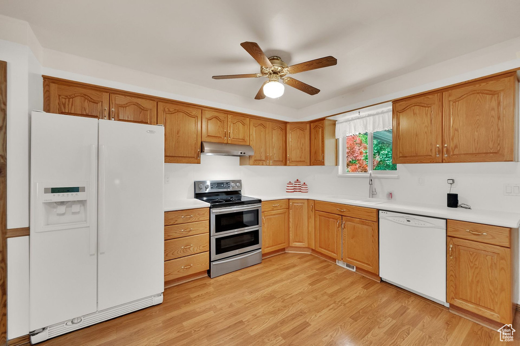 Kitchen with white appliances, under cabinet range hood, a ceiling fan, light countertops, and light wood finished floors