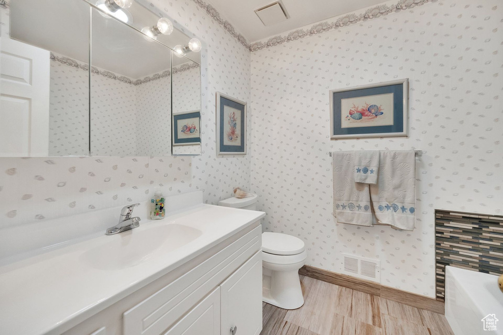 Full bath with a bathtub, vanity, wood finished floors, and wallpapered walls